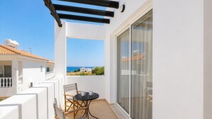 Ein Balkon mit Tisch und Stühlen, Blick auf das Meer und ein weißes Gebäude mit Ziegeldach.