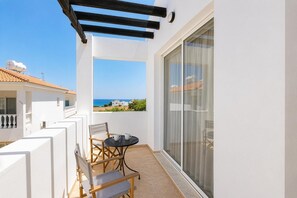 Ein Balkon mit Tisch und Stühlen, Blick auf das Meer und ein weißes Gebäude mit Ziegeldach.