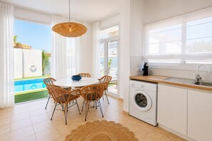 Eine moderne Küche mit integriertem Waschmaschinenanschluss, ein Essbereich mit Korbstühlen und Blick auf einen Swimmingpool.