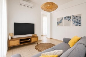 Un salon moderne avec un téléviseur à écran plat, un canapé gris, une table d’appoint en osier et un tapis en fibres naturelles.