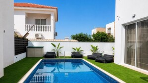 Ein rechteckiger Swimmingpool mit glasklar blauem Wasser, umgeben von künstlichem grünen Rasen, neben einem weißen Gebäude mit Balkon.