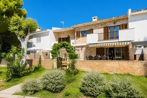 A two-story house with a stone facade, a balcony with outdoor seating, and a garden with various shrubs. - Villa Isleta - Four Bedroom Villa, Sleeps 8 (Mallorca)