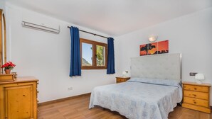 Ein Schlafzimmer mit einem Bett, einem Nachttisch, einer Kommode, einem Fenster mit Vorhängen und einer Wand-Klimaanlage.