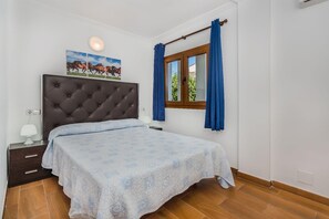A bedroom with a bed, a nightstand, a lamp, a window with curtains, and a wall-mounted picture. - Villa Isleta - Four Bedroom Villa, Sleeps 8 (Mallorca)