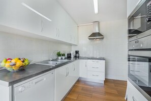 Uma cozinha moderna com armários brancos, uma coifa de aço inoxidável e um forno embutido.