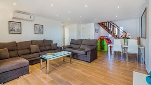 Ein Wohnzimmer mit einer Sofagarnitur, einem Glastisch, einer Treppe und einem Essbereich mit Stühlen und Tisch.