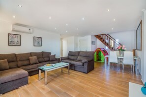 Ein Wohnzimmer mit einer Sofagarnitur, einem Glastisch, einer Treppe und einem Essbereich mit Stühlen und Tisch.