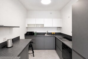Eine moderne Küche mit grauen Schränken, einer schwarzen Arbeitsplatte, einem Wasserkocher, einem Toaster und einem Spülbecken.