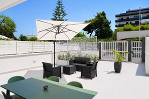 An outdoor patio area with a dining table, chairs, a sofa, and an umbrella. - GuestHost - Comfy Verandah Flat X6 Near the Sea (Trani)