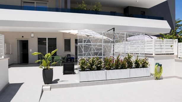A modern outdoor area with a white geometric fence, potted plants, and a hose. - GuestHost - Comfy Verandah Flat X6 Near the Sea (Trani)