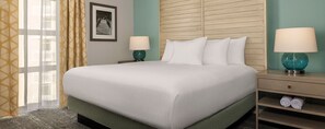 Ein Hotelzimmer mit einem großen Bett, zwei Nachttischlampen, einem gerahmten Bild an der Wand und einem Fenster mit Vorhängen.