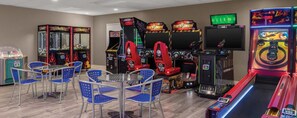Ein Spielhallenambiente mit verschiedenen Spielautomaten, blauen Stühlen und einem Fernsehbildschirm.