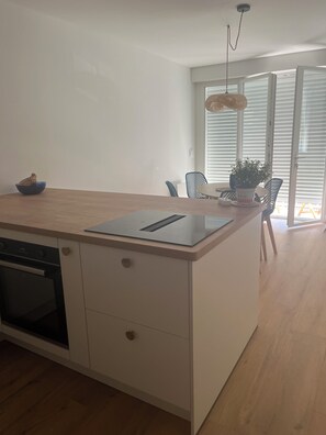 A modern kitchen with a built-in oven, a wooden countertop, and a dining area with chairs and a table. - Fully renovated apartment. Perfect for a couple. Close to amenities, the beach, and a park. (Arcachon)
