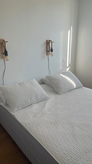 A bedroom with two beds, each with white bedding and pillows, and a wooden wall-mounted light fixture. - Fully renovated apartment. Perfect for a couple. Close to amenities, the beach, and a park. (Arcachon)