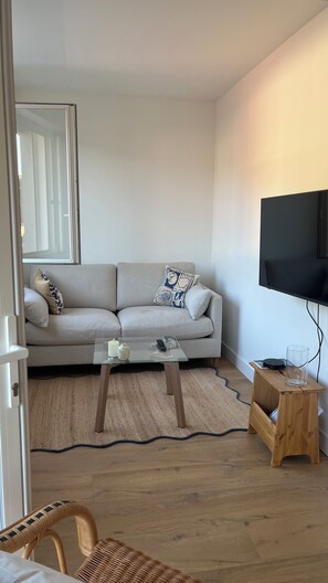 A living room with a sofa, a coffee table, a television, and a small wooden table. - Fully renovated apartment. Perfect for a couple. Close to amenities, the beach, and a park. (Arcachon)