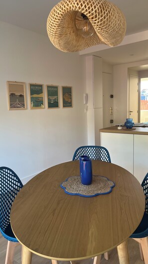 A round wooden dining table with a blue vase, surrounded by blue chairs with a woven placemat. - Fully renovated apartment. Perfect for a couple. Close to amenities, the beach, and a park. (Arcachon)
