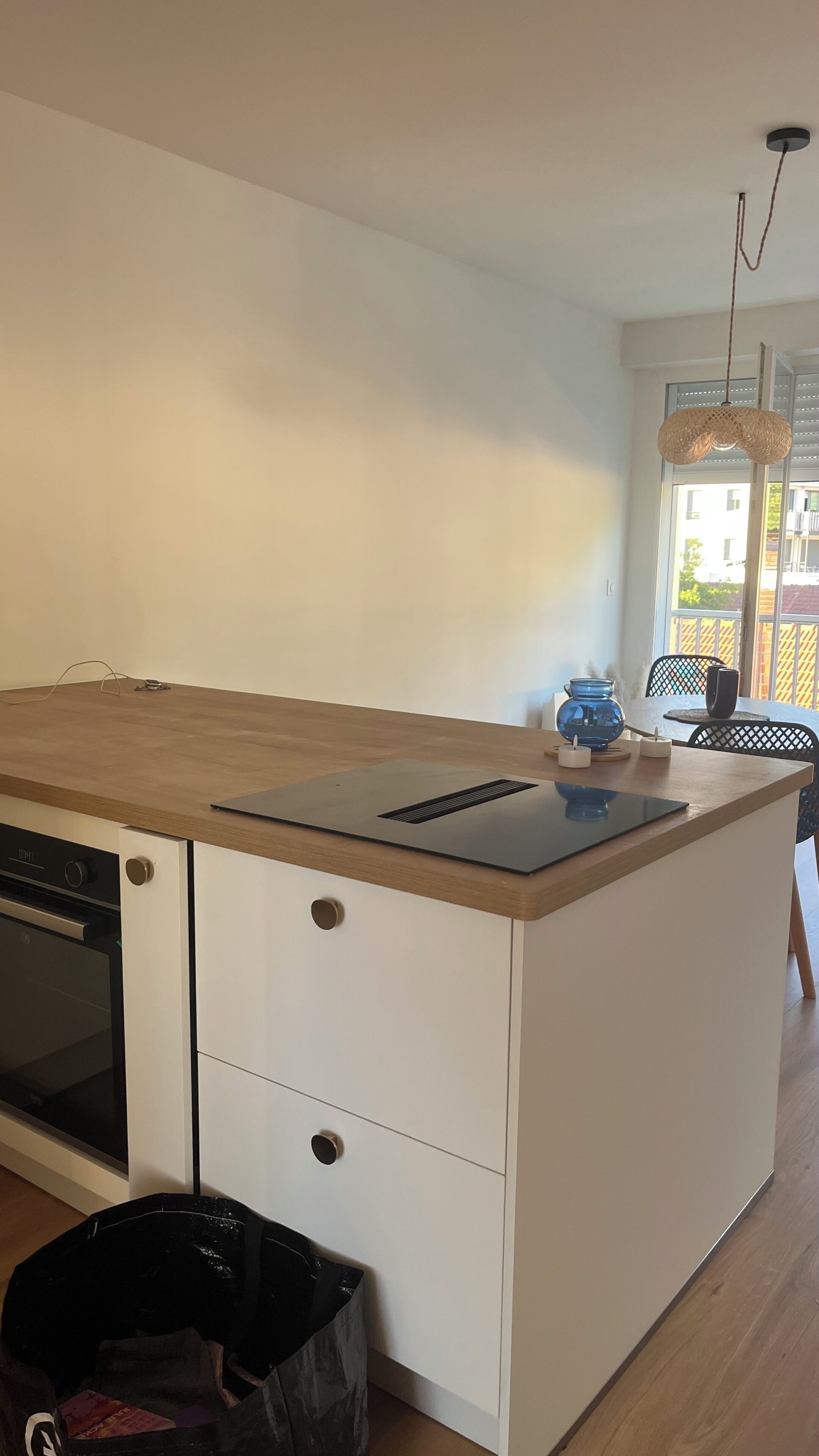 Een moderne keuken met een houten aanrecht, een ingebouwde oven, witte kastjes en uitzicht op het buitengebied door een raam.