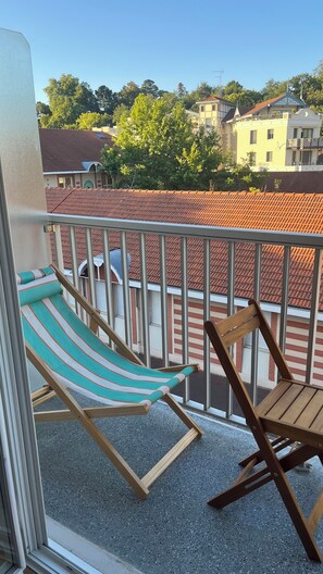 A balcony with a striped hammock and wooden chairs, overlooking a residential area with red-tiled roofs. - Fully renovated apartment. Perfect for a couple. Close to amenities, the beach, and a park. (Arcachon)