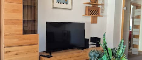 Una sala de estar moderna con un mueble de entretenimiento de madera, un televisor de pantalla plana, una obra de arte enmarcada y una planta en maceta.