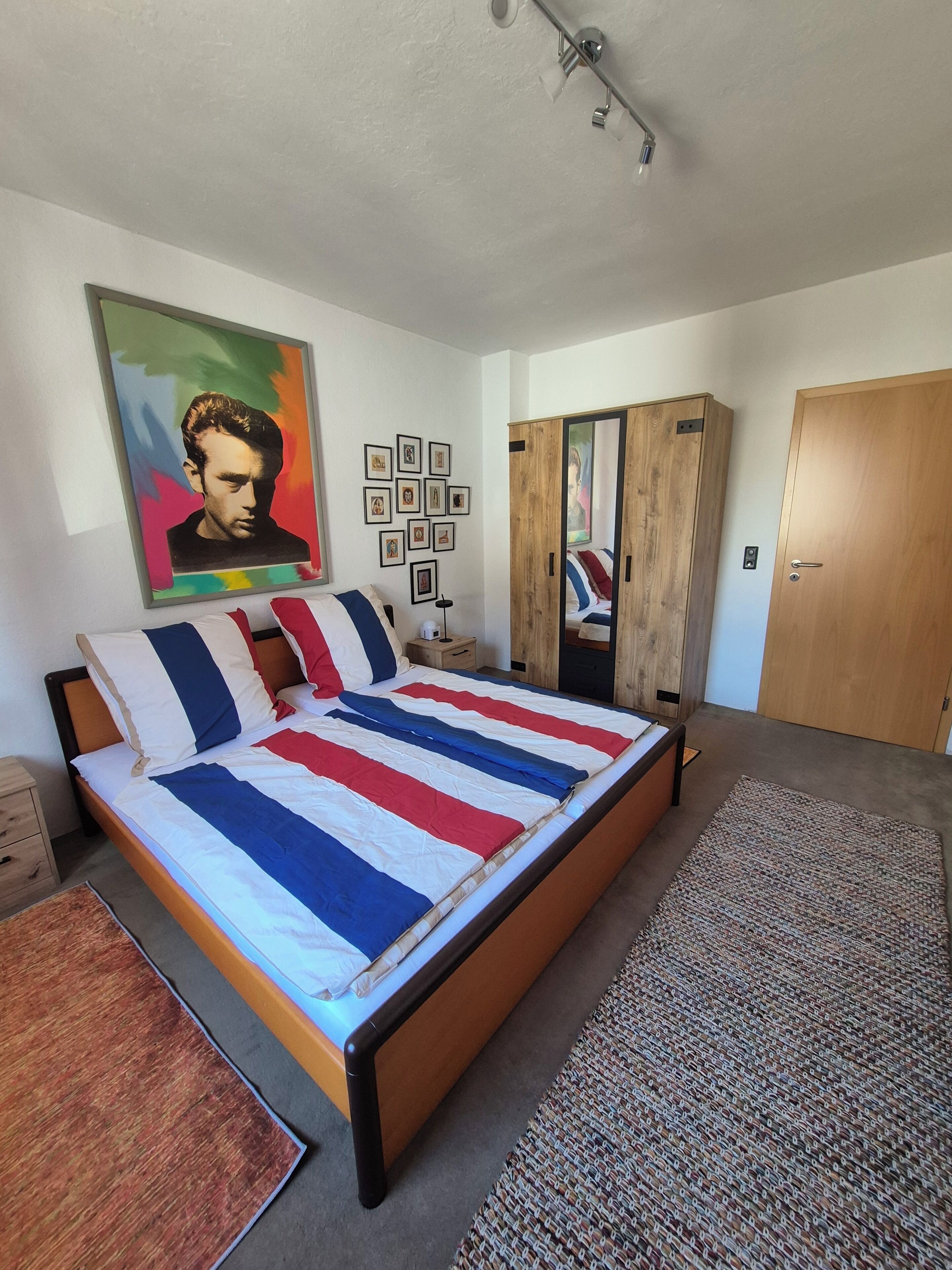 Ein Schlafzimmer mit einem Bett, einem Kleiderschrank, einem Spiegel und einem Bild an der Wand.