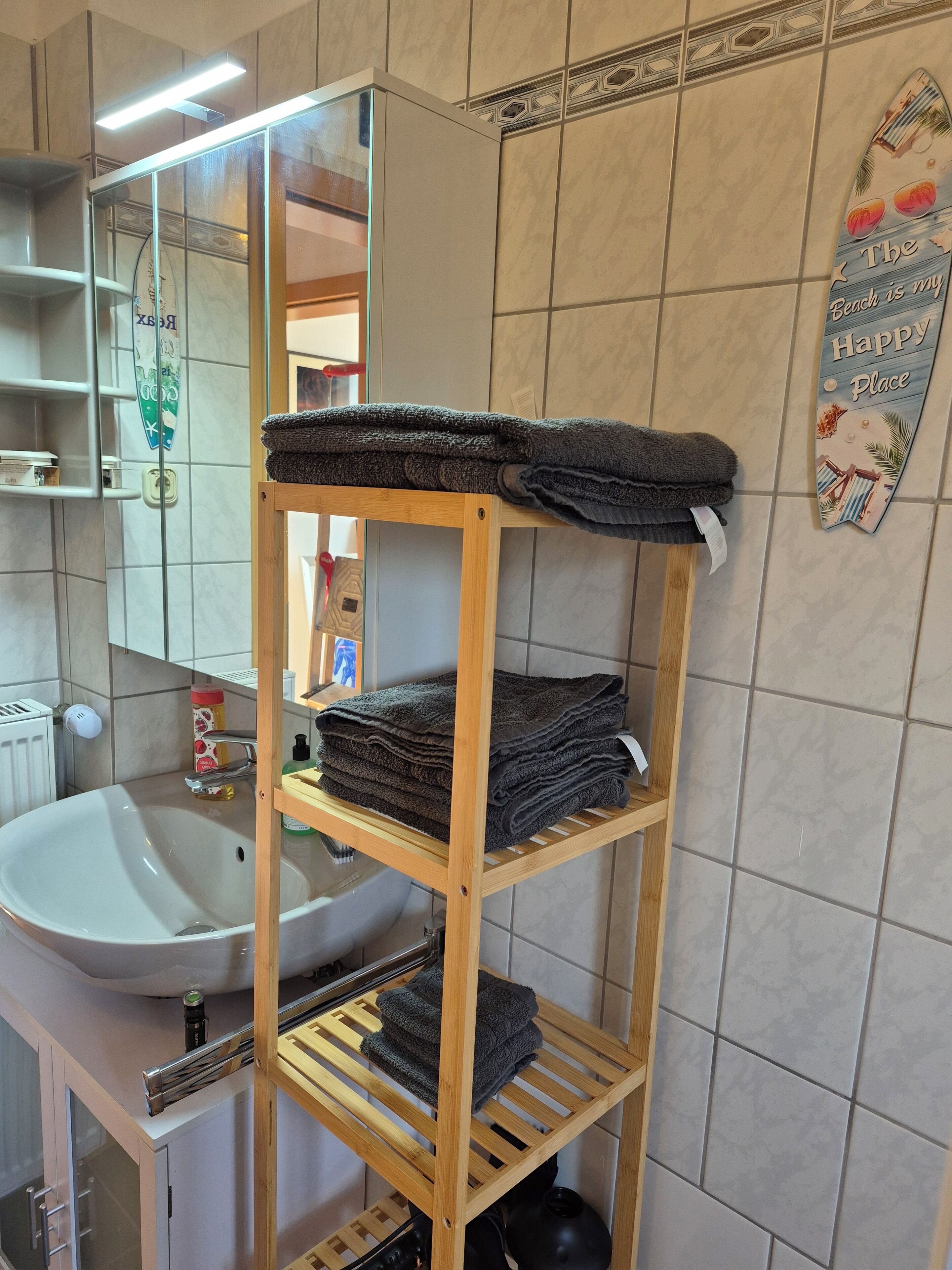 Une salle de bain avec une étagère en bois où sont pliées des serviettes, un lavabo et un miroir.