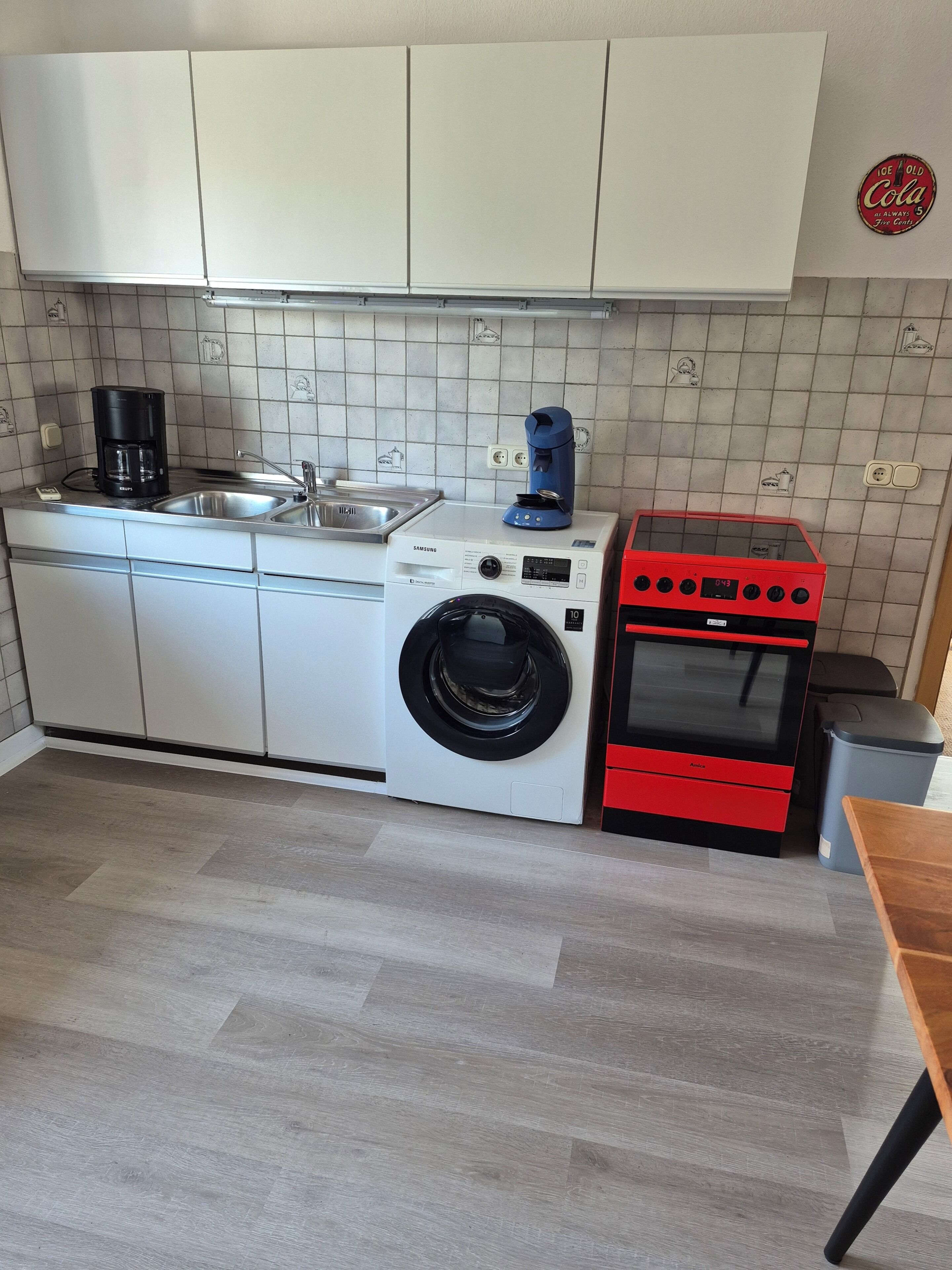 Eine kleine Küche mit Waschmaschine, Kaffeemaschine und einem roten Backofen.