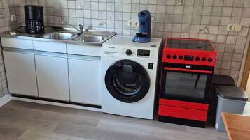 Eine kleine Küche mit Waschmaschine, Kaffeemaschine und einem roten Backofen.