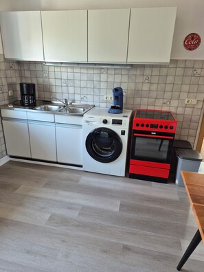 Una cocina compacta con lavadora, cafetera y horno rojo.