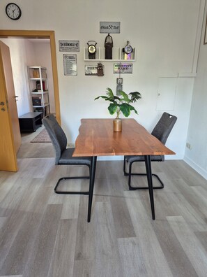 A dining area with a wooden table and black metal chairs, a potted plant, and various wall decorations including clocks and signs. - Tranquil 1-bedroom apartment in Oberhausen for a relaxing stay (Oberhausen)