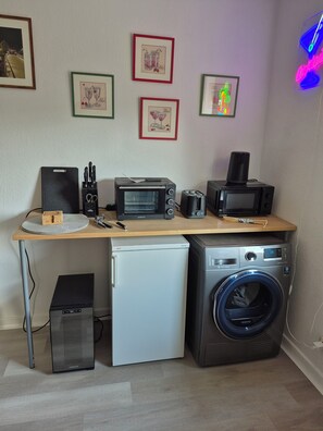 Eine kompakte Küchenzeile mit Toaster, Mikrowelle, kleinem Kühlschrank und Waschmaschine.