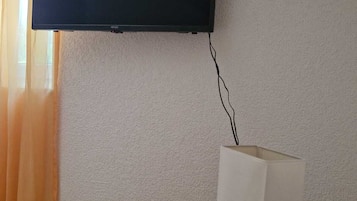 Et fjernsyn monteret på en væg, en fjernbetjening på et træbord, og en lampe med hvide skærm.