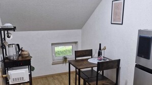 A compact kitchen with a dining table, chairs, a small window, and a refrigerator. - Duvnjak Rooms (Livno)