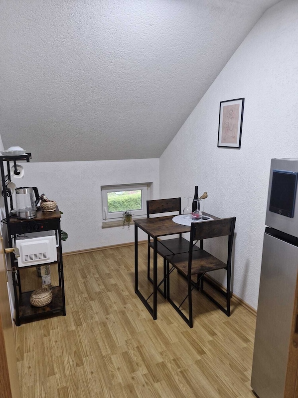 A compact kitchen with a dining table, chairs, a small window, and a refrigerator.