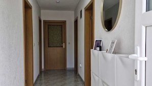 A hallway with a tiled floor, wooden doors, a white cabinet with a mirror, and a door with a textured glass panel. - Duvnjak Rooms (Livno)