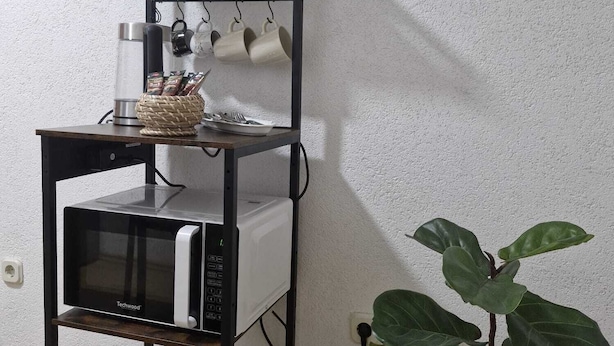 A kitchen area with a black metal shelf unit holding a microwave, a glass jar, and a basket. - Duvnjak Rooms (Livno)