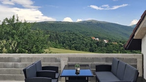 An outdoor seating area with wicker furniture, a table, and a view of a green landscape with hills. - Duvnjak Rooms (Livno)