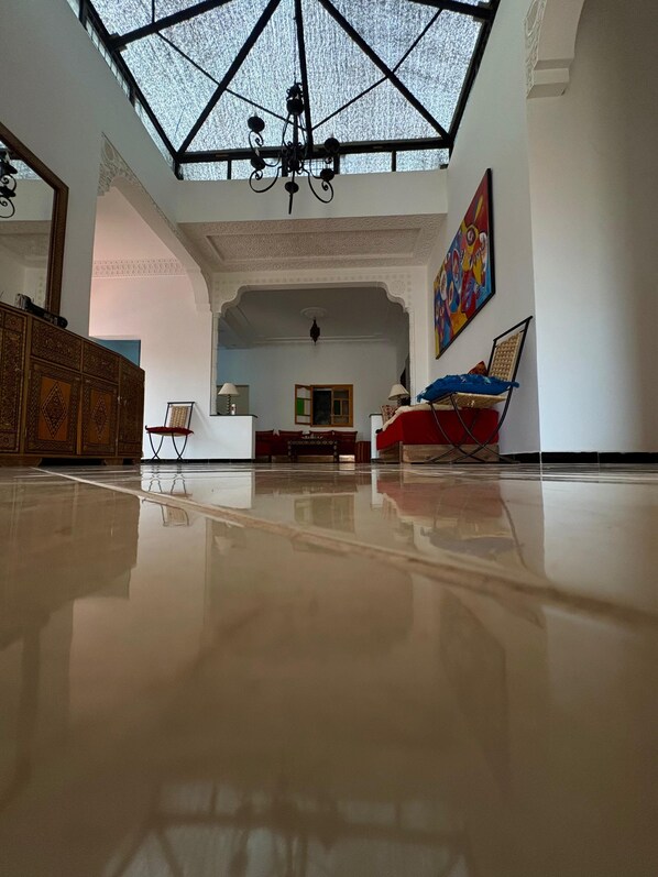 A spacious room with a high ceiling, a chandelier, a large painting, and a polished floor.