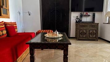 A living room with a red sofa, a glass-top coffee table, a cabinet with decorative items, and a flat-screen TV mounted on the wall.