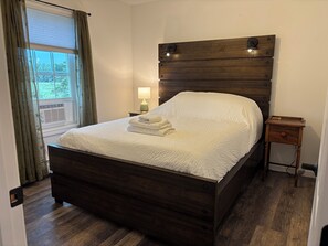 Een netjes opgemaakt bed met een hoofdbord, een bedlampje en een klein houten nachtkastje met een lade.