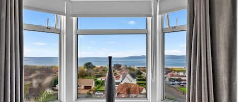 A bay window with a clear view of a coastal landscape, including houses and the sea.