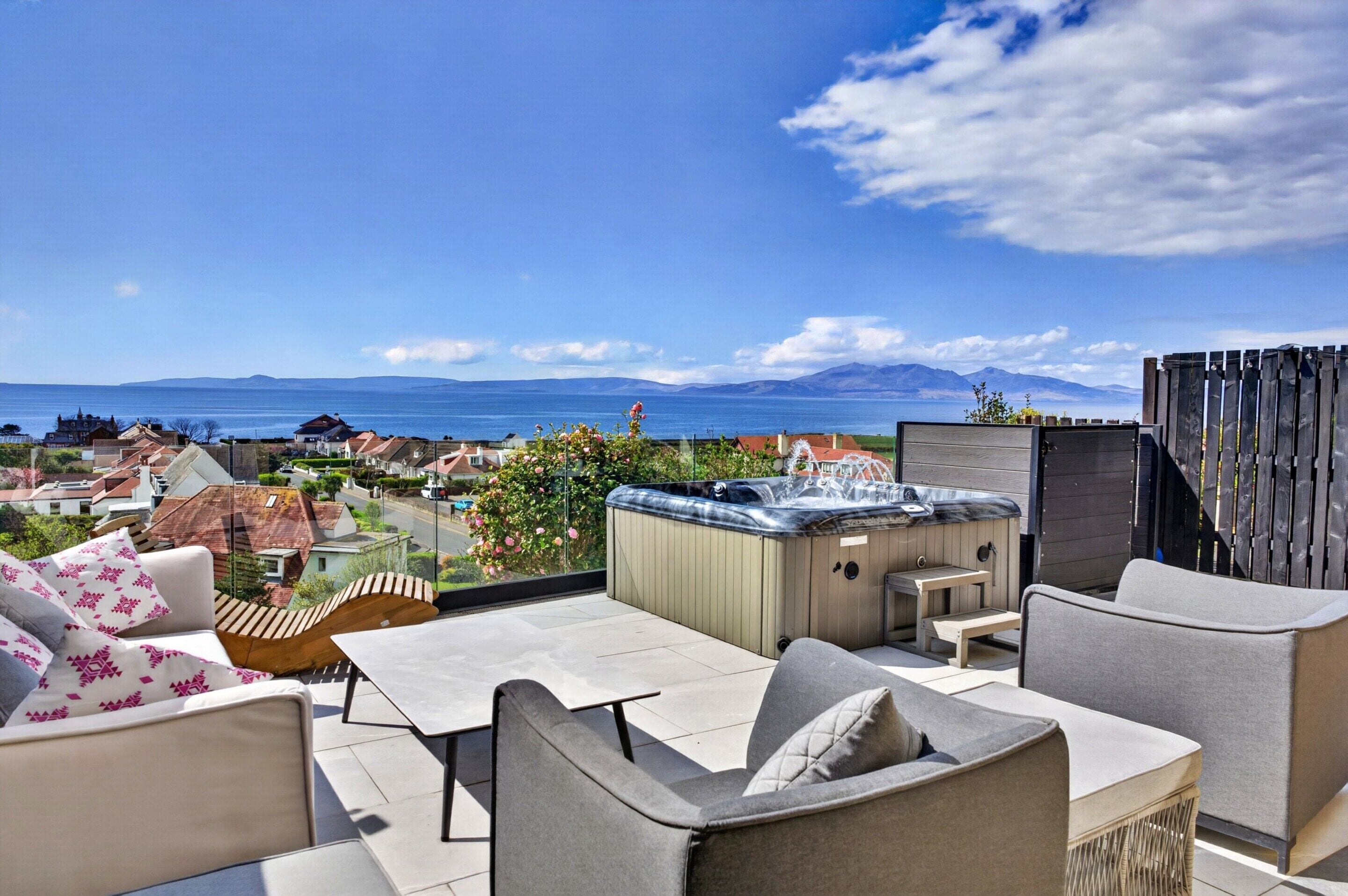 A rooftop terrace with outdoor seating, a hot tub, and a view of the sea and mountains.