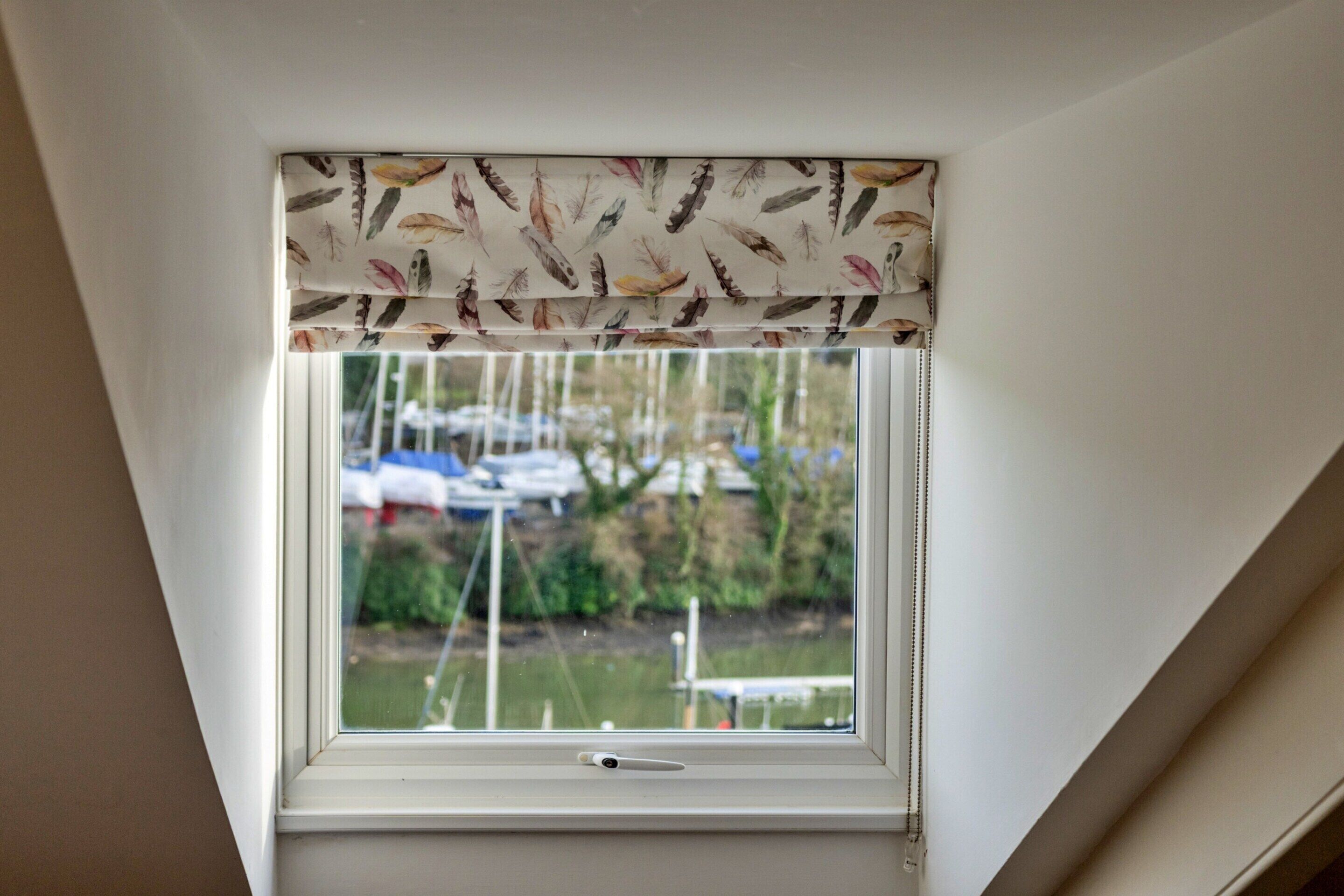 A skylight with a white frame and a window with a curtain featuring a feather pattern.