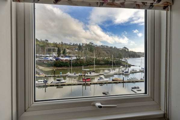 Vista attraverso una finestra su un porto turistico con barche ormeggiate, un cielo sereno e un paesaggio collinare sullo sfondo.