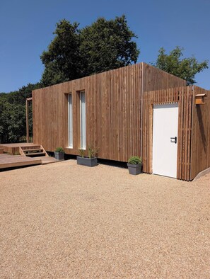 A modern wooden building with a white door, large windows, and a gravel driveway. - The Landaoudec Cabin (Crozon)