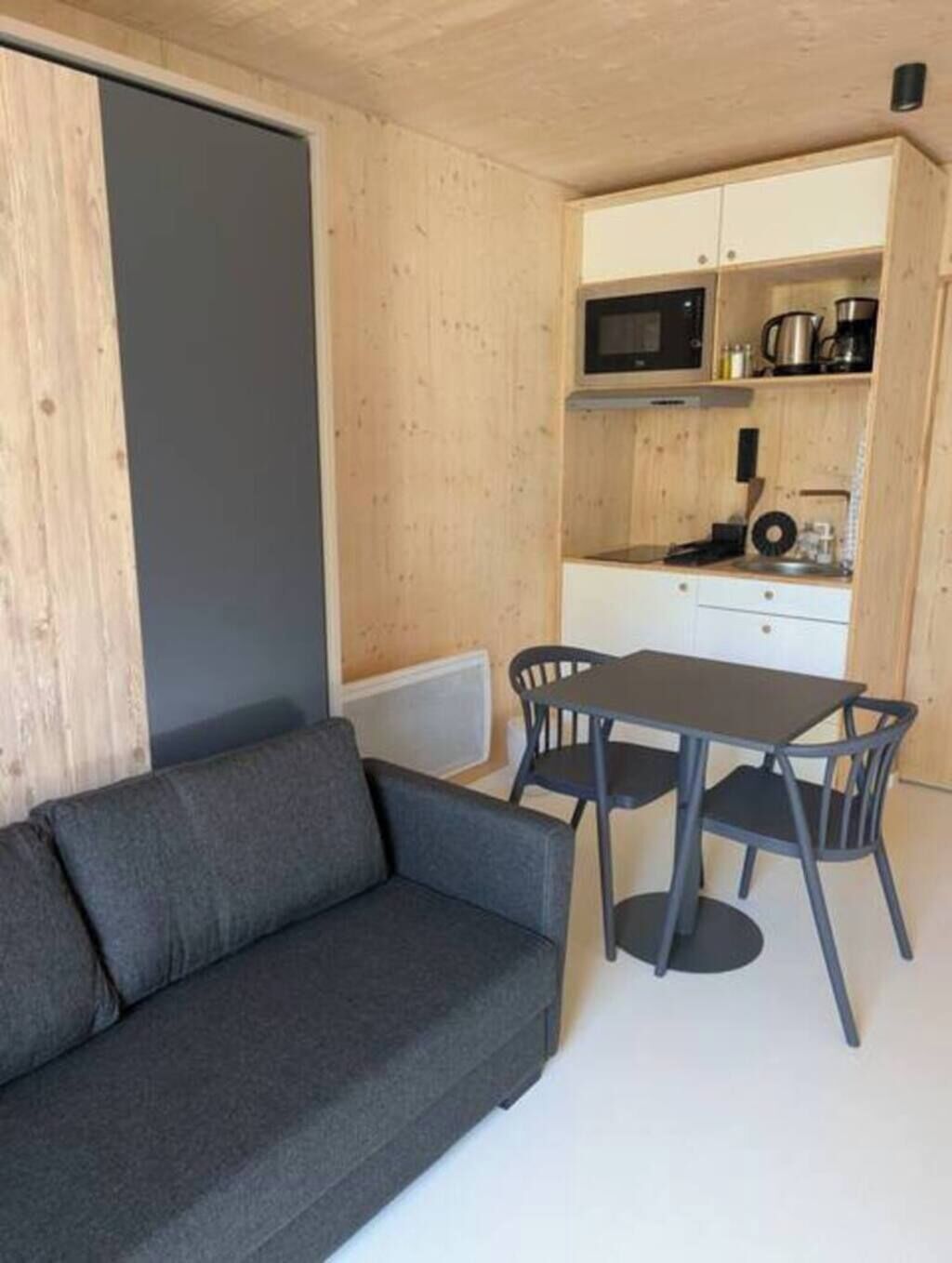 Ett kompakt bostadsutrymme med en soffa, ett matbord med stolar och en liten köksdel med mikrovågsugn och kaffebryggare.