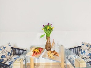 A dining area with a table set for two, featuring a fruit platter, croissant, and a vase with flowers. - Apartment Sleeps 4 Enclosed Garden Pets Welcome (Falmouth)