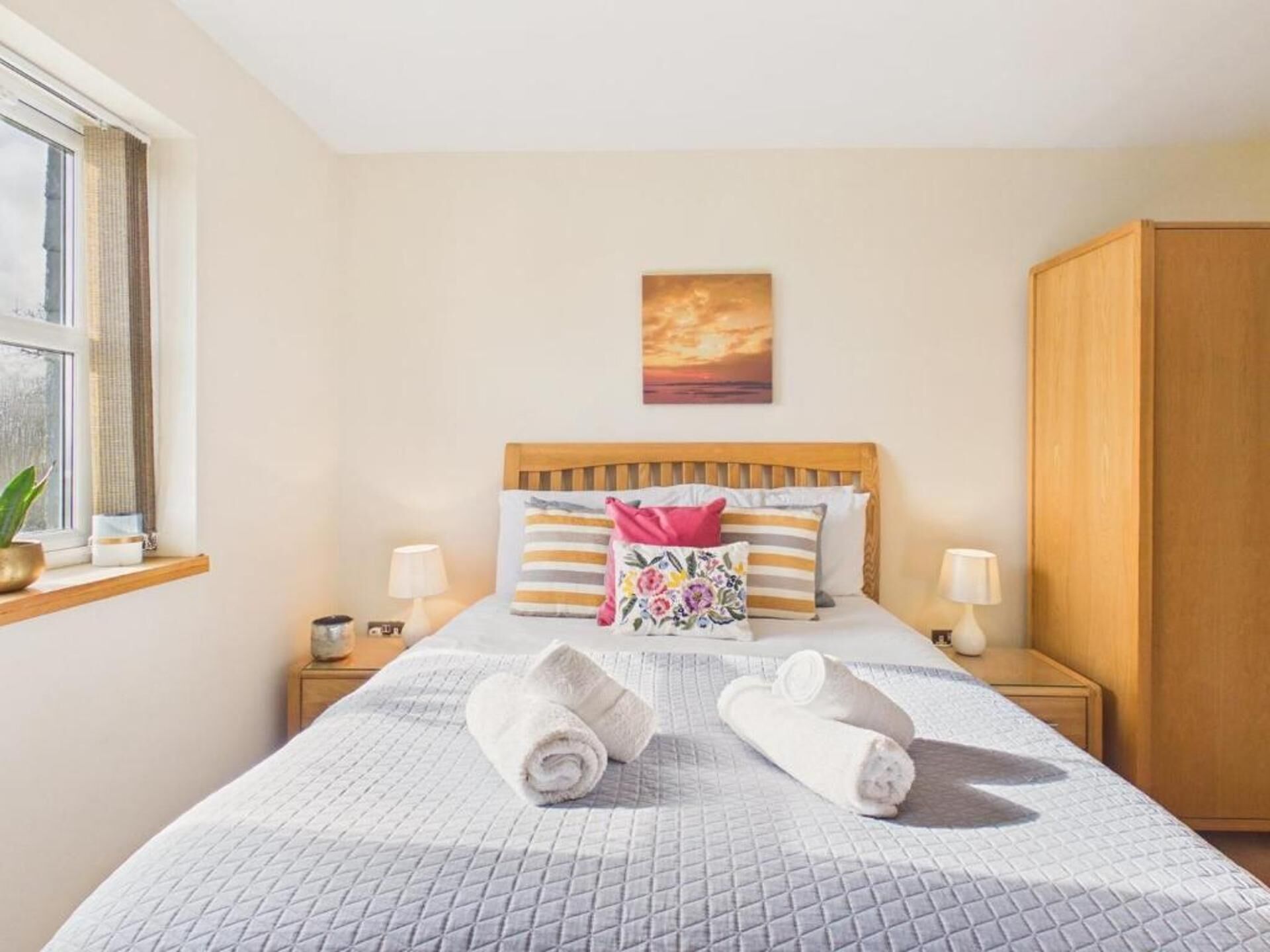 Une chambre d’hôtel avec un lit, deux tables de chevet, une fenêtre avec des rideaux, une armoire en bois et un tableau au mur.