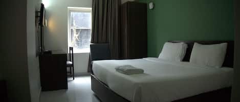 Habitación de hotel con cama, escritorio, silla y ventana con cortinas.