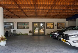 A building entrance with a wooden ceiling, a glass door, and a paved driveway. - Hotel Golden Heights international (Ernakulam)