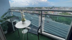 Een balkon met een tafel en stoelen, een bloempot en uitzicht op een stadsbeeld met wegen en gebouwen.